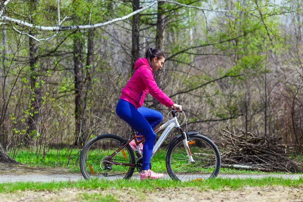woman in a bright pink jacket and jeans rides a bike