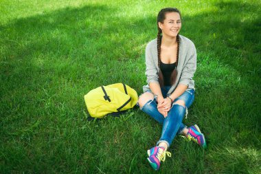 Yeşil çimenlerin üzerinde bir şehir parkta oturan genç kadın 