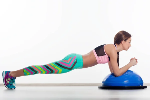 A dark-haired woman coach in a sporty short top and gym leggings makes legs  with dumbbells on a rug for yoga, on a summer day in a park on a green la