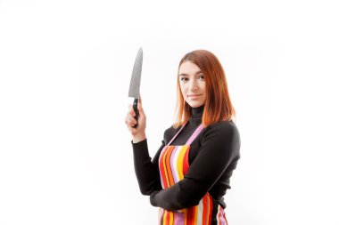 Kızıl saçlı bir kadın siyah bir balıkçı yaka ve poz ve bir beyaz izole arka plan üzerinde bir büyük mutfak bıçağı tutan bir mutfak önlüğü