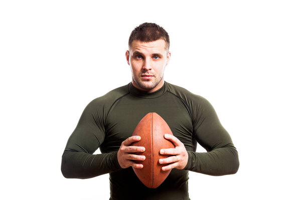A young dark-haired male wrestler in a green sports rashgard smiles and holds a rugby ball in the hands of a white isolated background