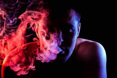 Genç bir adam siyah bir izole rengi kırmızı ve pembe renk renkli duman bulutu exhales. Elektronik Sigara Buhar admiting puffs biri. 