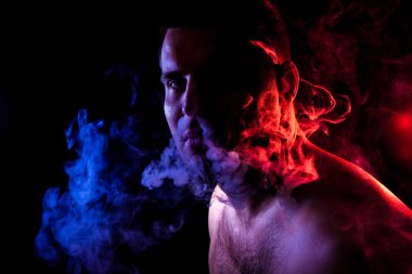 Genç bir adam hepsini geri kaplıdır siyah bir izole rengi mavi ve kırmızı renk renkli duman ile kırmızı duman bulutu exhales. Genç bir hırsız örneği içinde sigara içmek için zarar