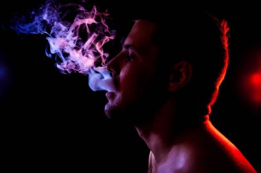 Genç bir adam siyah bir izole rengi kırmızı, mavi ve pembe renk renkli duman bulutu exhales. Elektronik Sigara Buhar admiting puffs biri. 