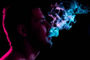 Genç bir adam siyah bir izole rengi kırmızı ve yeşil renk renkli duman bulutu exhales. Elektronik Sigara Buhar admiting puffs biri. 