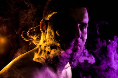 Genç bir adam hepsini geri kaplıdır siyah bir izole rengi sarı ve mor renk renkli duman ile sarı duman bulutu exhales. Genç bir hırsız örneği içinde sigara içmek için zarar