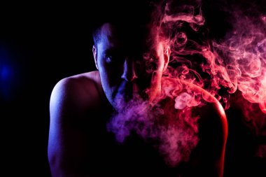 Genç bir adam siyah bir izole rengi kırmızı ve mavi renk renkli duman bulutu exhales. Elektronik Sigara Buhar admiting puffs biri. 