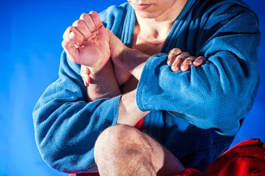 Close-up two wrestlers of grappling and jiu jitsu in a blue and red kimono makes armbar .Submission wrestling   on blue tatami clipart