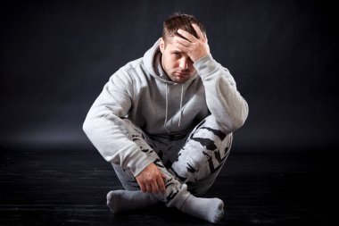 Bir genç, üzgün görünümlü adam spor giysileri yere oturuyor ve üzgün, tcho, onun başım ağrıyor, elleri siyah izole arka plana tutuyorsun ağartılmış esmer,.