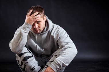 Bir genç, üzgün görünümlü adam spor giysileri yere oturuyor ve üzgün, tcho, onun başım ağrıyor, elleri siyah izole arka plana tutuyorsun ağartılmış esmer,.