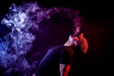 Gri bir şapka ve siyah tişört exhales pembe siyah yalıtılmış zemin elektronik sigara dumanı kadar genç bir adam