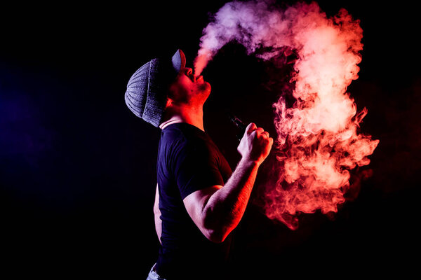 Vaping man holding a mod. A cloud of vapor. Black background. Vaping an electronic cigarette with a lot of smoke. Vape concept