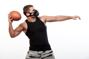 Genç bir erkek atlet siyah eğitim maskeli bir spor gömlek beyaz izole arka planda bir ragbi topu tarafından sallanır