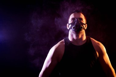 Mavi bir vape duman çevresinde siyah yalıtılmış zemin üzerine spor gömlek ve eğitim maskesi giyen genç atletik adam portresi