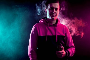 Spor hoody vaping elektronik sigara adam. Siyah arka plan üzerine izole. Pembe ve yeşil duman bulutları