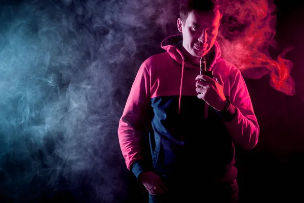 Man in sport hoody vaping an electronic cigarette.Isolated on black background.Around  clouds of smoke