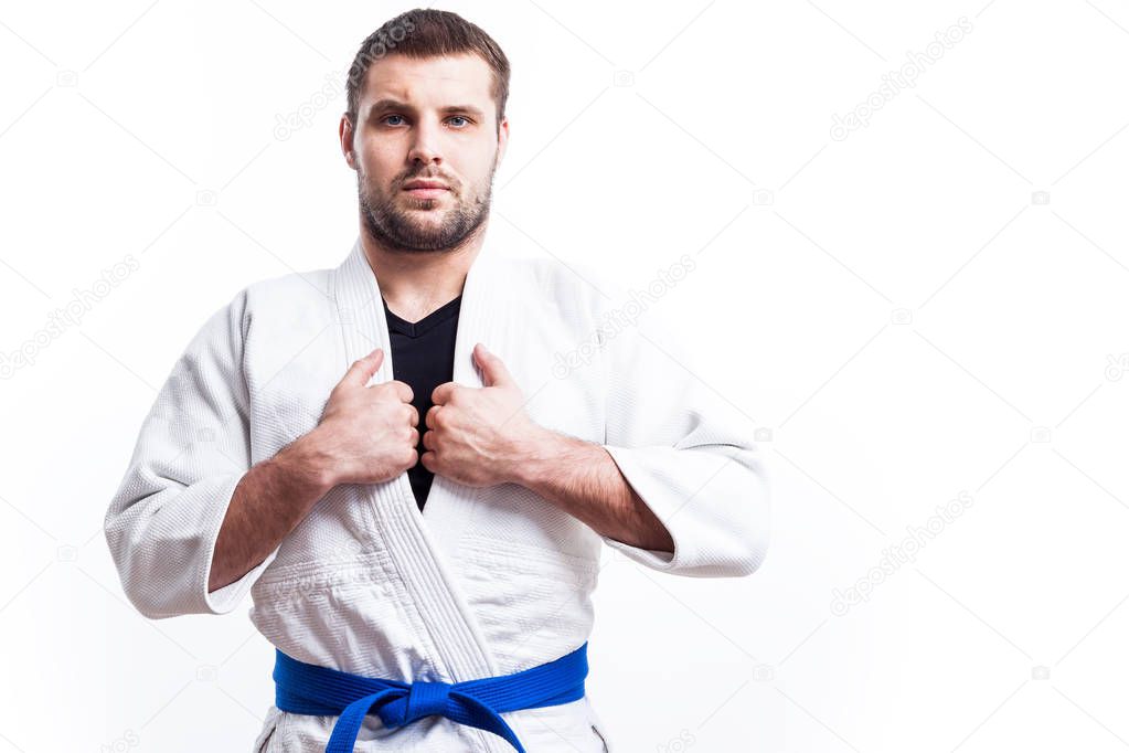 A young athletic man is a fighter in a white kimono for judo, jiu jitsu, sambo with a blue belt standing on a white isolated background