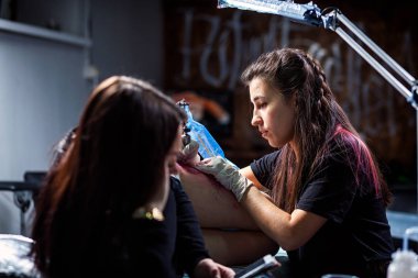 Kadın profesyonel dövmeci dövme kırmızı boyalar baştankara küçük bir kuş karanlık dövme salonunda, yan görünüm çekici bir kadın yapıyor