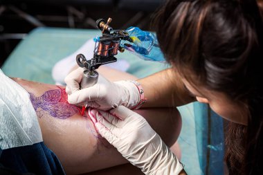A close-up of the process of creating a bird tattoo by a female tattoo master on a hip under sterile conditions clipart