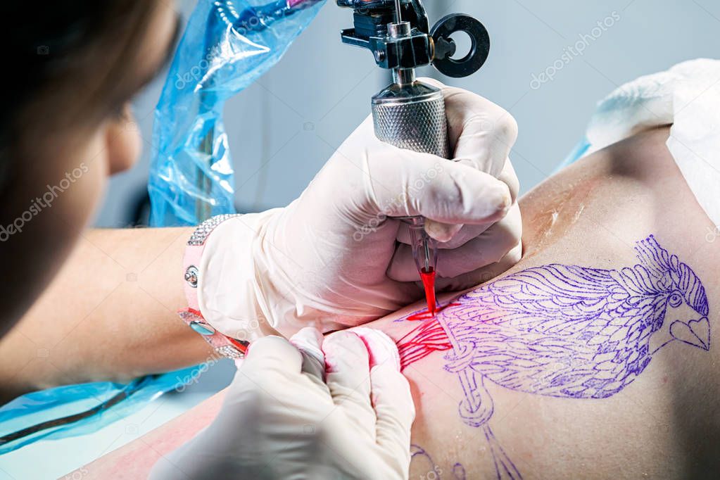 Tattoo artist during tattooing bird a client on the femur