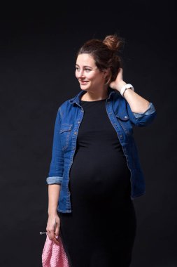 Genç esmer güzel kadın gülümseyerek ve siyah bir izole arka plan üzerinde poz gözlük ve kot gömlek geç gebelik üzerinde