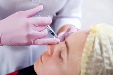 Bir güzellik Close-Up elmacık kemikleri içine Botox enjeksiyon tıbbi ofis formunda düzeltmek için genç bir kadın enjekte eder.