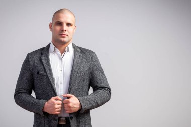 Genç bir kel adam beyaz gömlekli, gri takım güvenle kameraya bakar ve ceketini izole beyaz bir arka plan üzerinde onun ellerini tutar
