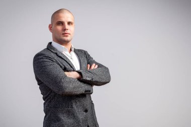 Genç bir kel adam beyaz gömlekli, gri takım güvenle kameraya bakar ve kollarını göğsünde izole beyaz bir arka plan üzerinde çarpı işareti tutar