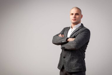 Genç bir kel adam beyaz gömlekli, gri takım güvenle kameraya bakar ve kollarını göğsünde izole beyaz bir arka plan üzerinde çarpı işareti tutar