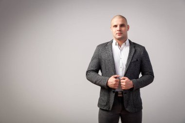 Genç bir kel adam beyaz gömlekli, gri takım güvenle kameraya bakar ve ceketini izole beyaz bir arka plan üzerinde onun ellerini tutar