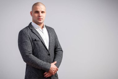 Genç bir kel adam beyaz gömlekli, gri takım kesinlikle kameraya bakar ve ceketini izole beyaz bir arka plan üzerinde onun ellerini tutar