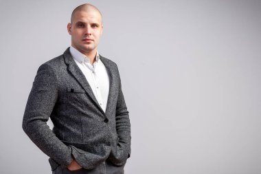 Genç bir kel adam beyaz gömlekli, gri takım kesinlikle kameraya bakar ve elleri ceplerinde ceketinin beyaz izole arka planda tutar
