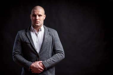 Genç bir kel adam beyaz gömlekli, gri takım güvenle kameraya bakar ve ceketini izole siyah bir arka plan üzerinde onun ellerini tutar
