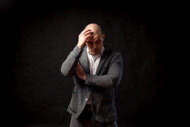 Beyaz bir gömlek bir kel adam işadamı, gri takım elbise standları ve izole bir siyah arka plan üzerine bir problem çözme hakkında düşünüyor