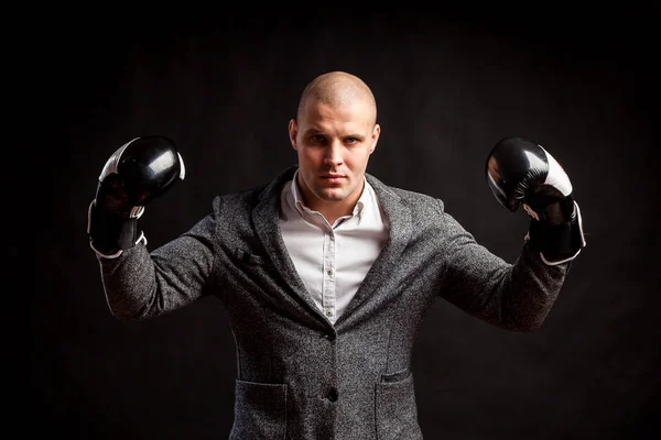A young man manager in a white shirt, gray suit, boxing gloves looks seriously and show biceps  on a black isolated background