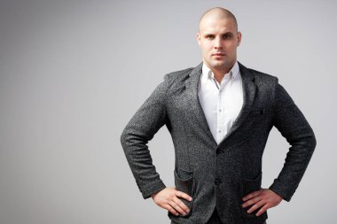 Genç bir kel adam beyaz gömlekli, gri takım güvenle kameraya bakar ve ceketini izole beyaz bir arka plan üzerinde onun ellerini tutar