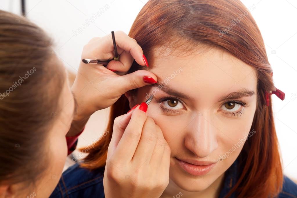 Close-up of the eyebrow is the perfect shape of the eyebrows, plucking eyebrows tweezers before staining a young red-haired woman on a white isolated background, front view