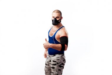 Sportif delikanlı mavi Taytlı, siyah dirsek ve eğitimler maskesi duruyor ve bir beyaz izole arka plan üzerinde başparmak ortaya