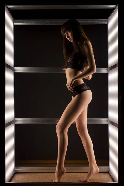 黒のレースのランジェリーを暗い部屋で明るいランプの中でポーズの若い黒髪女性 — ストック写真