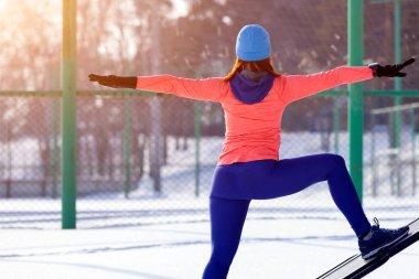 Genç kadın bir parlak mavi şapka, turuncu kazak eğitimi bir spor alanında bir parlak kış günü. Fitnesss tren kış orman