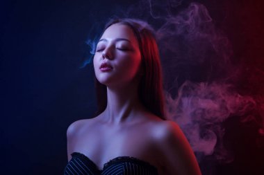 Asyalı genç kadın bir vape siyah yalıtılmış zemin üzerinden gözlerini kapatma ve kırmızı ve mavi bir arka planda poz duman