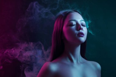 Asyalı genç kadın bir vape siyah yalıtılmış zemin üzerinden gözlerini kapatma ve kırmızı ve mavi bir arka planda poz duman
