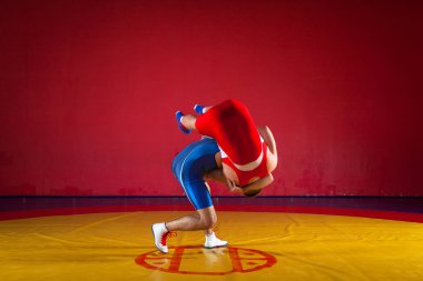 Two strong wrestlers in blue and red wrestling tights are wrestlng and making a suplex wrestling on a yellow wrestling carpet in the gym. Young man doing grapple. clipart