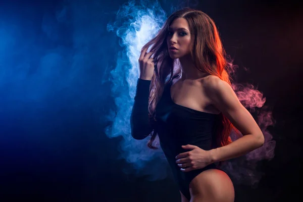 Young dark-haired woman in black underwear posing against a background of  blue smoke from a vape on a black isolated background