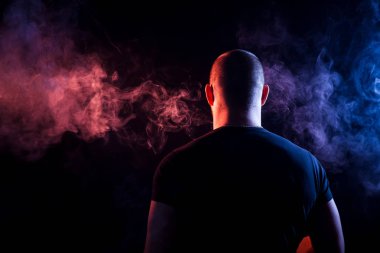 Genç bir adam siyah bir izole rengi kırmızı ve mavi renk renkli duman bulutu exhales. 