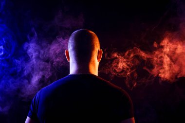 Genç bir adam siyah bir izole rengi kırmızı ve mavi renk renkli duman bulutu exhales. 