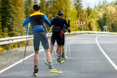 Takım biotlonists spor malzemeleri içinde Koruyucu baretler eller Kayak Polonyalılar tutmak silindir kayaklar, Altay dağlık alanda bir yaz gününde orman boyunca asfalt yol boyunca kayak gitmek