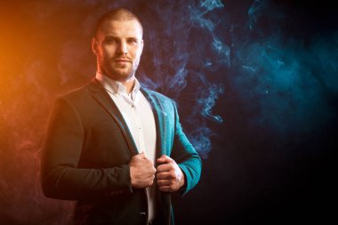 Genç yakışıklı adam Yöneticisi Beyaz gömlekli gülümsüyor ve kırmızı ve mavi mendil izole siyah arka plan üzerine gelen duman karşısında yeşil ceket düzeltiyor