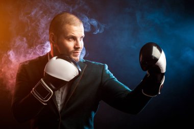 Yakışıklı sporcu içinde beyaz gömlek, yeşil ceket, siyah ve beyaz boks eldiven boks ve kırmızı ve mavi duman siyah yalıtılmış zemin temizleme işlemi üzerinden herhangi bir ters mücadele için hazır...