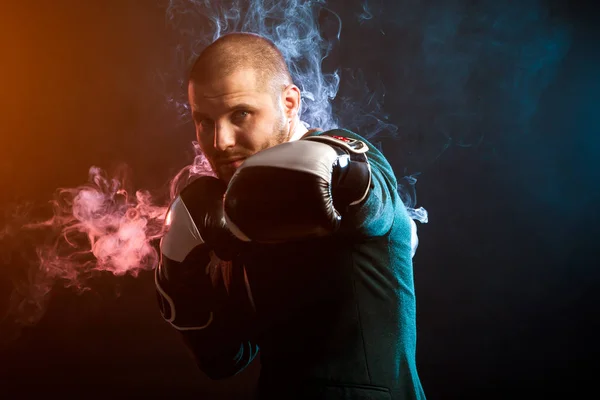 Handsome man sportsman in white shirt, green jacket, black and white boxing gloves boxing and ready to tackle any opposite of red and blue smoke from a wipe on a black isolated background...